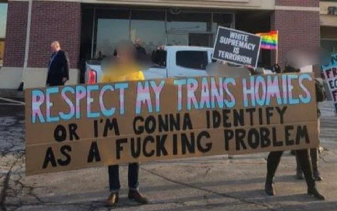 two anonymous people holding a sign that says “respect my trans homies or I’m going to identify as a problem”